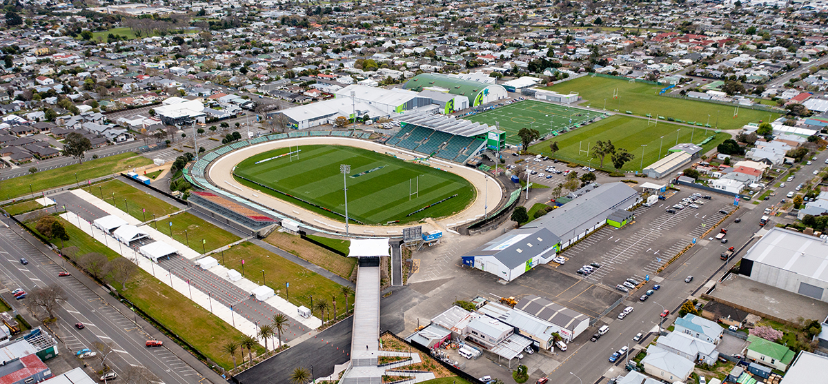 Multiple rugby fields seen from high angle view. The field in the foreground is surrounded by a racetrack and there is a stadium seating area on the far side