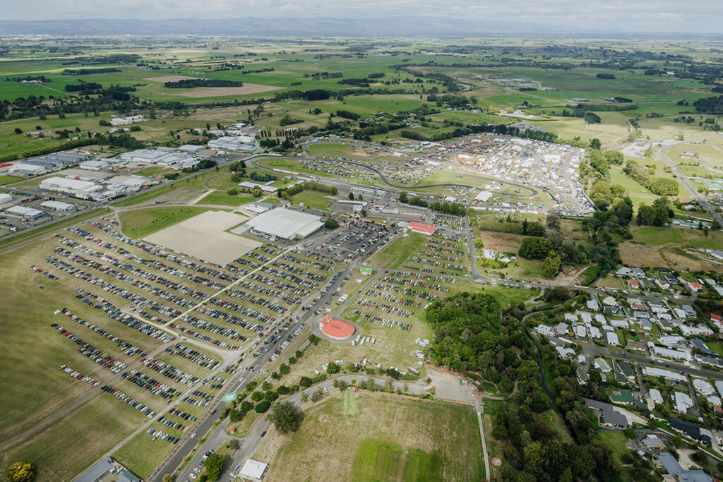 Aerial photograph of a green landscape with many parked cars and a racing track visible in the middle distance